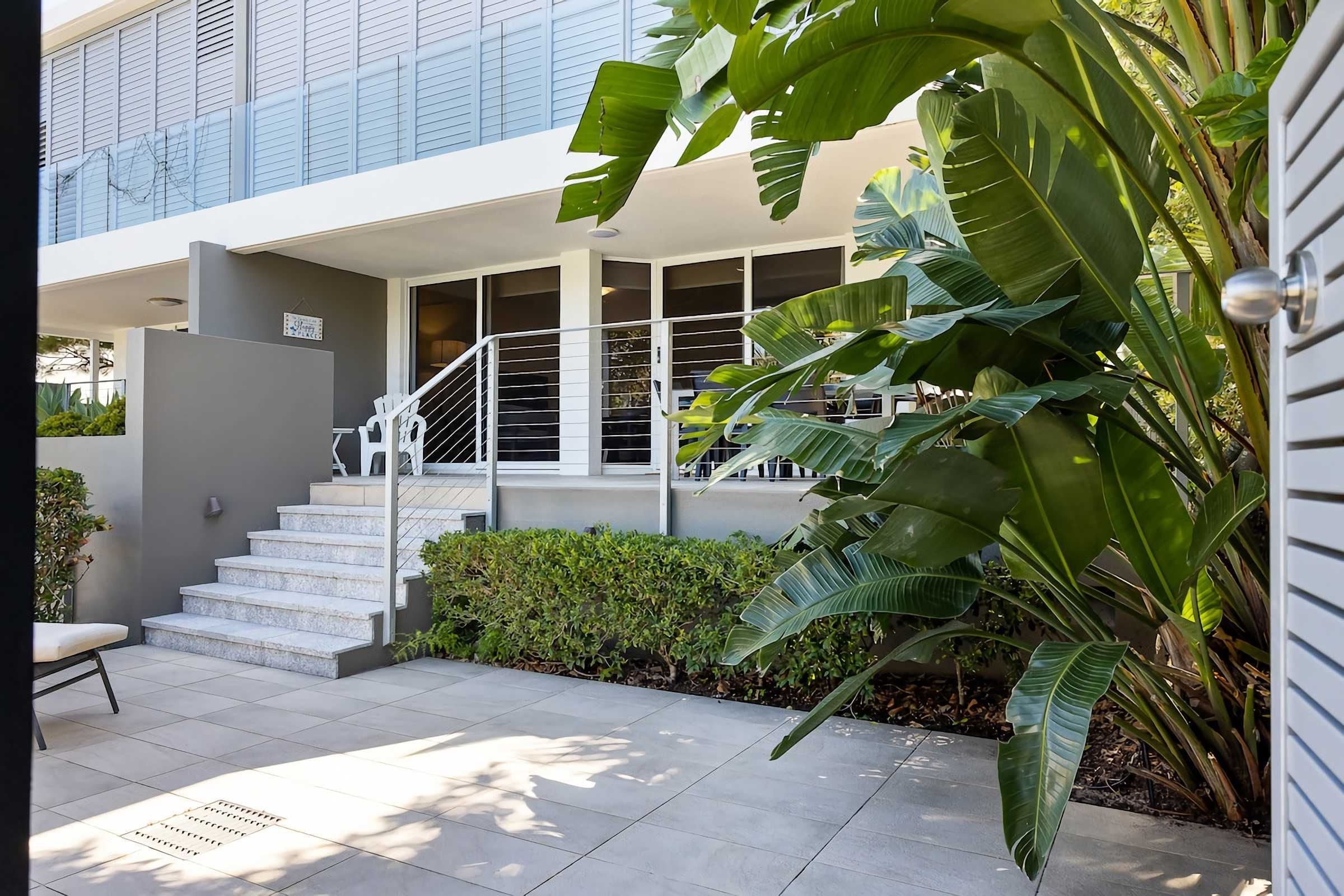 Un edificio moderno con una escalera que lleva a un acceso cubierto, rodeado de vegetación.