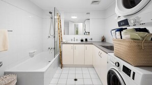 Une salle de bain moderne équipée d’une baignoire, d’une douche, d’un lavabo et d’un lave-linge.