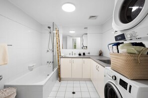 A modern bathroom with a bathtub, shower, sink, and a washing machine. - The Sunshine Villa 2 Min walk to Village Beach (Noosa)