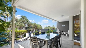 Une terrasse extérieure avec une table et des chaises, entourée de verdure et sous un ciel dégagé.