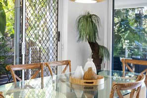 A glass-top dining table with wooden chairs, a decorative plant, and a tray with vases. - The Sunshine Villa 2 Min walk to Village Beach (Noosa)