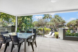 A covered outdoor dining area with a glass table and chairs, surrounded by lush greenery and palm trees. - The Sunshine Villa 2 Min walk to Village Beach (Noosa)
