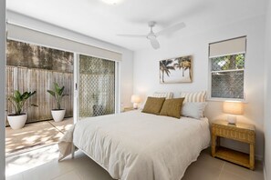 A bedroom with a bed, two bedside tables with lamps, a ceiling fan, a window with a view, and a wall-mounted artwork. - The Sunshine Villa 2 Min walk to Village Beach (Noosa)