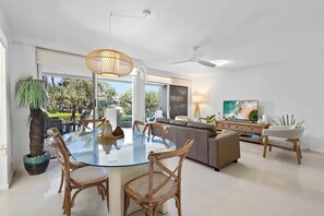 A modern living room with a glass dining table, comfortable seating, a large TV, and a view of the outdoors. - The Sunshine Villa 2 Min walk to Village Beach (Noosa)