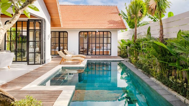 Une maison moderne dotée d’une piscine, d’une terrasse en bois et de plantes tropicales.