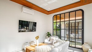 Un salon moderne avec un plafond en bois, une grande fenêtre à cadre noir, un canapé blanc, une table basse et un téléviseur fixé au mur.