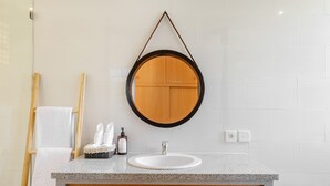 Une salle de bain avec un miroir rond, un lavabo, un meuble en bois, un porte-serviettes et une plante.