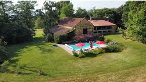 Una casa de piedra con piscina, rodeada de césped cuidado y árboles.