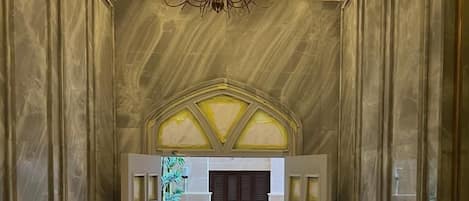 A hallway with a herringbone floor, a chandelier, and a door with glass panels.