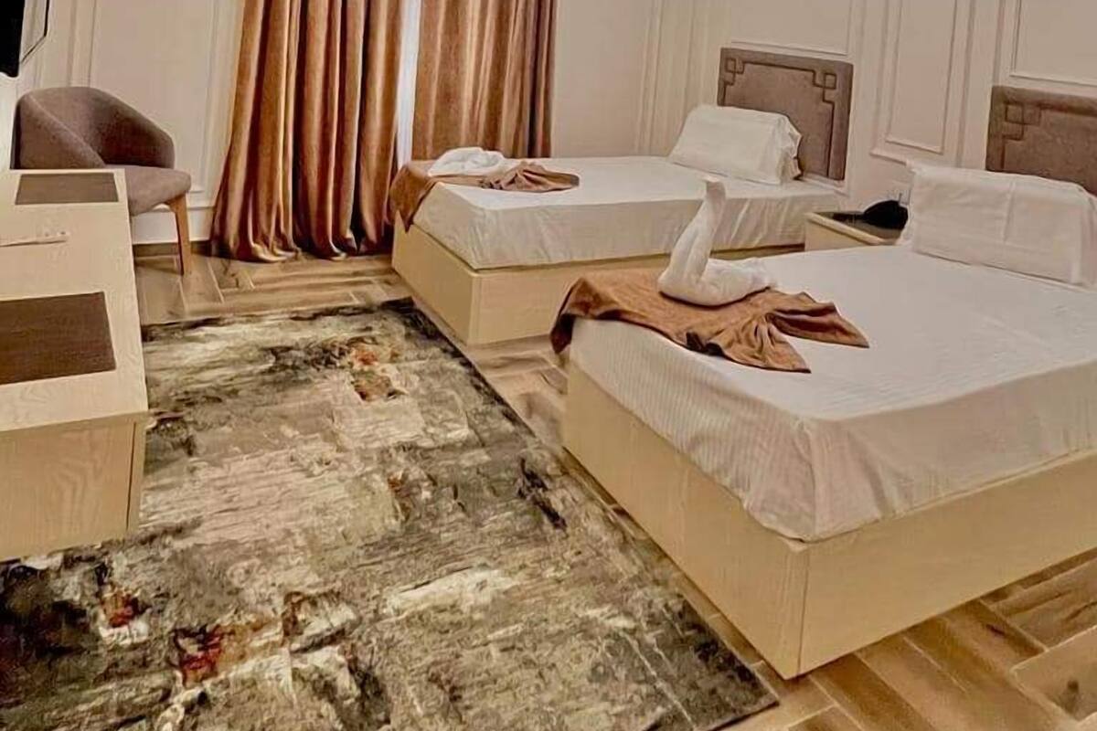 A hotel room with two beds, a desk, a chair, a TV, and a ceiling light fixture.