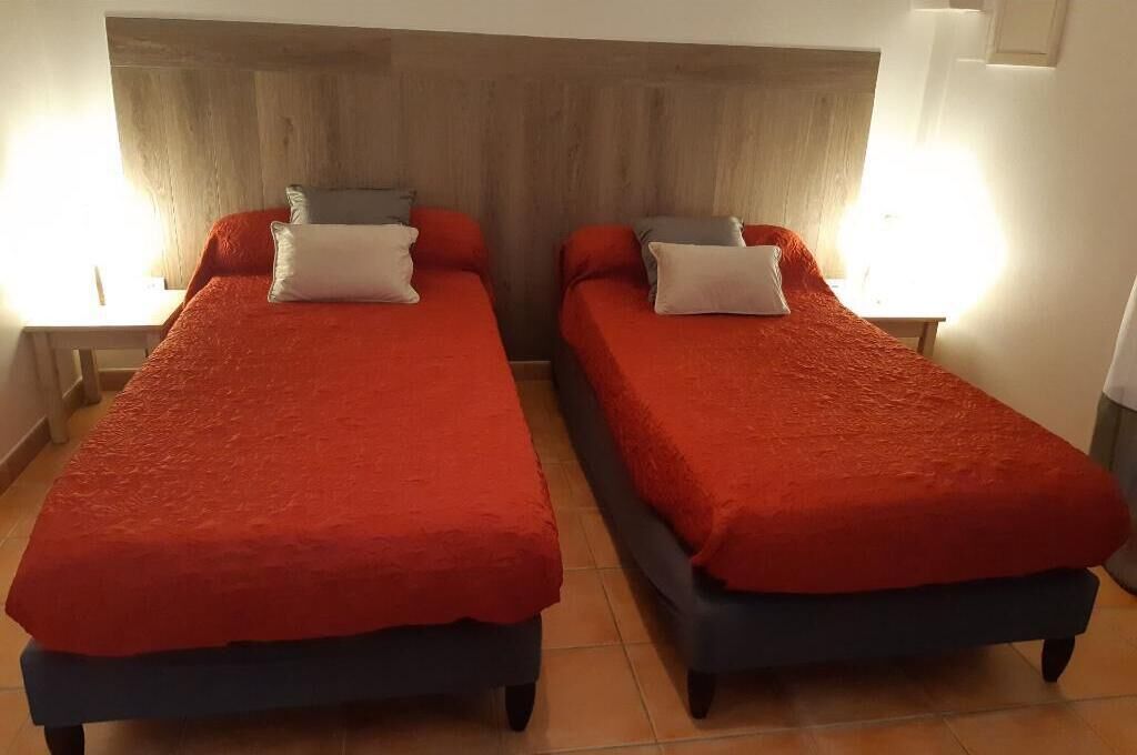 Deux lits simples avec une literie rouge, une tête de lit en bois et des lampes de chevet.