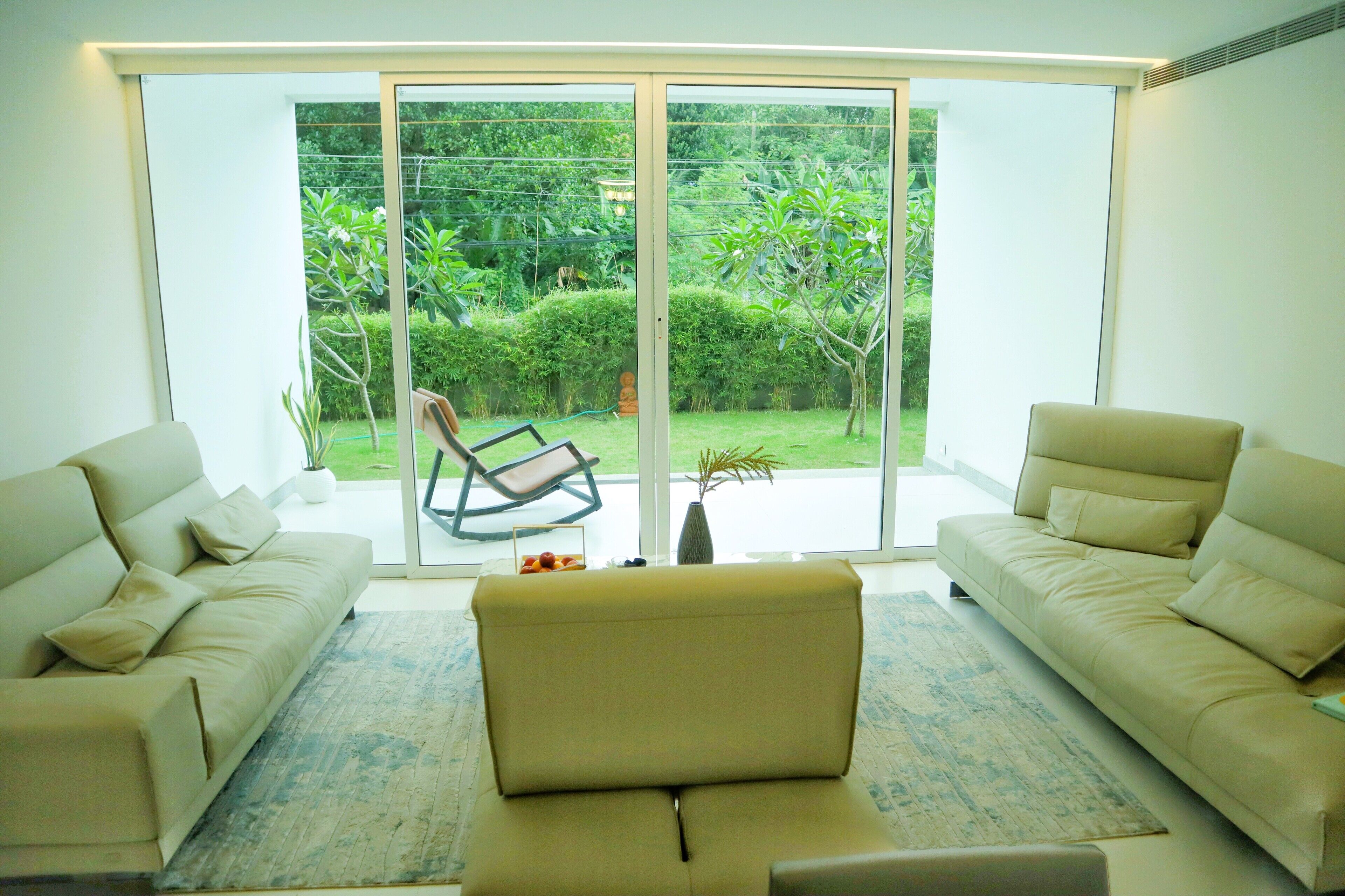 A modern living room with a large sliding glass door leading to a garden. There are two beige sofas and a small coffee table.