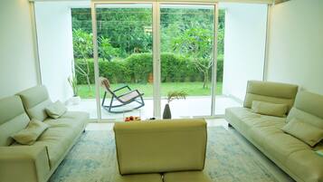 Una sala de estar moderna con un gran ventanal corredera que da a un jardín. Hay dos sofás beige y una mesita de centro.