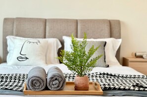A neatly made bed with a grey headboard, two rolled grey towels, and a small potted plant on a tray. - Amber Cove Impression City Heystay (Malacca City)