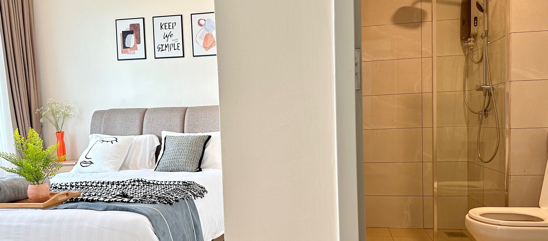A bedroom with a bed, pillows, a bedside plant, and a wall with framed artwork.