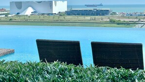 A pool with two chairs, a modern building, and a ship in the background.
