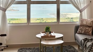 A room with a large window, a small round table with a tray, a sofa, and a patterned throw pillow.