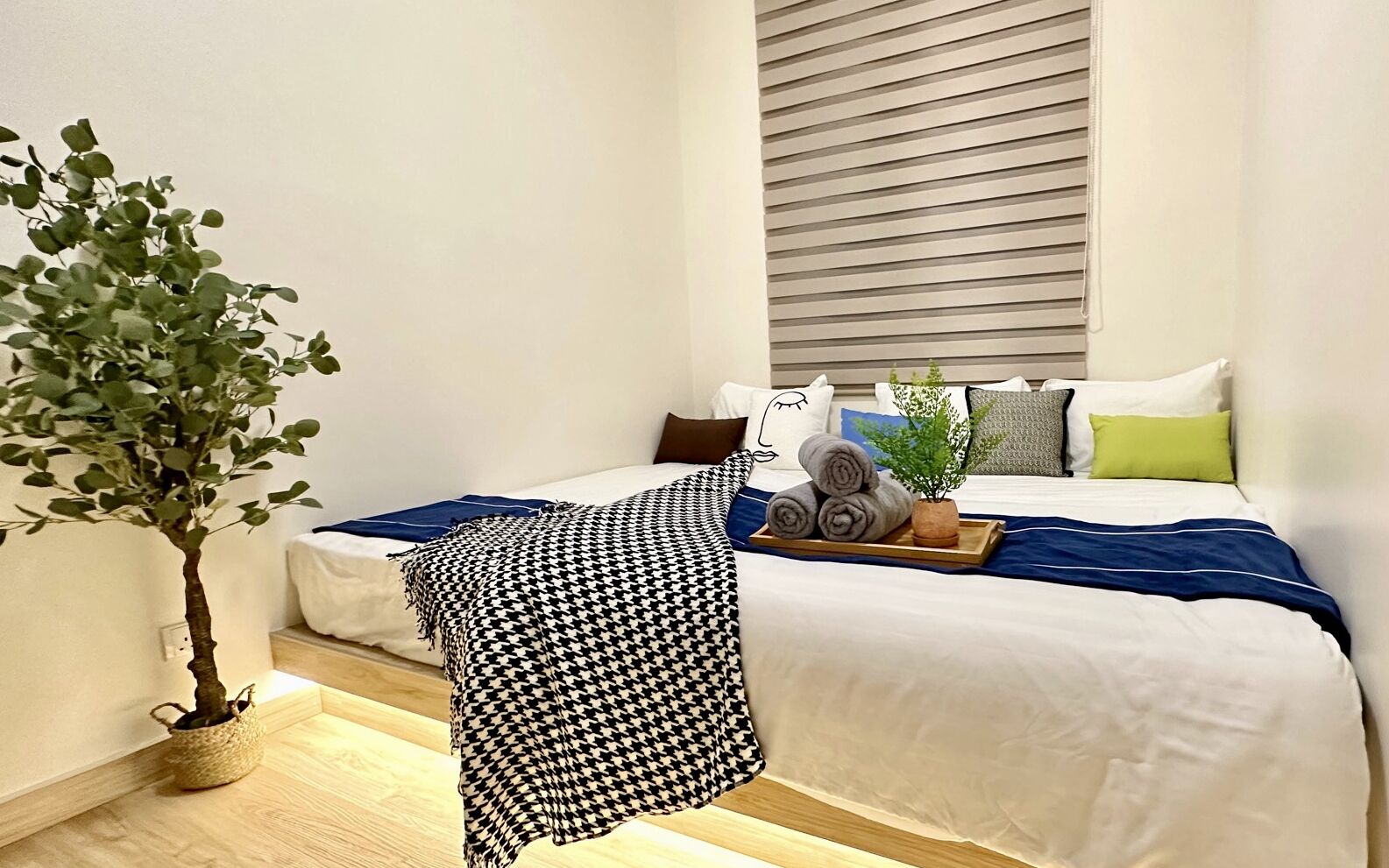 A modern hotel room with a neatly made bed, a small potted plant, and a tray with rolled towels.