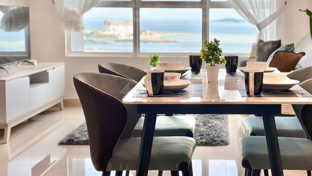 A modern dining area with a view of the sea, a dining table set with plates, cups, and a vase of flowers.