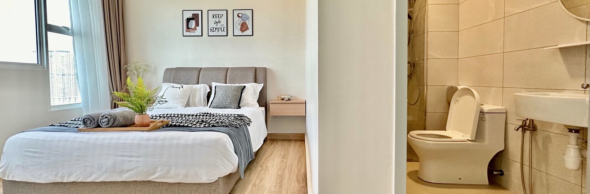 A neatly arranged bedroom with a bed, bedside table, and a view of the city through a window.