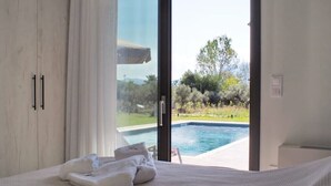 A bedroom with a large bed, a view of a swimming pool, and a door leading outside.