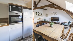 Una cocina equipada con microondas, horno y refrigerador. Hay un comedor con una mesa y sillas de madera. La habitación tiene vigas de madera a la vista en el techo.