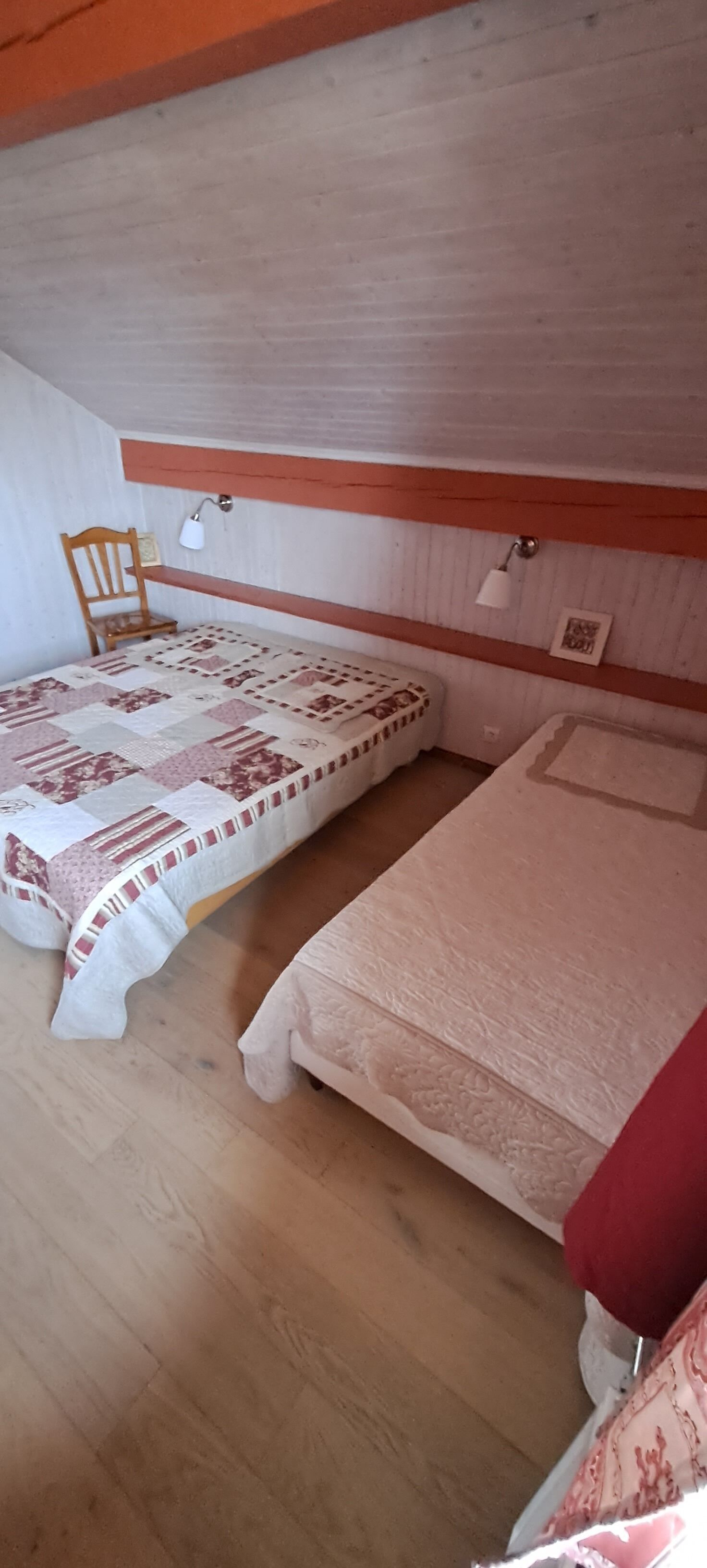 A bedroom with two beds, a wooden chair, and a shelf with a lamp.