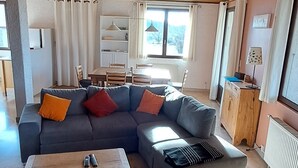 Een woonkamer met een hoekbank, een houten salontafel en een eethoek met een tafel en stoelen.