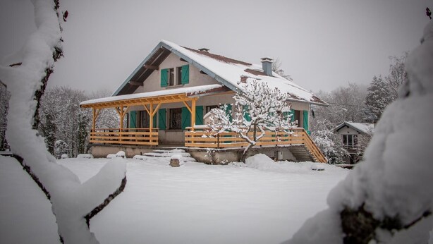 Een besneeuwde lodge met een houten veranda en een schoorsteen.