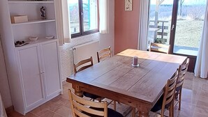 Een eethoek met een houten tafel en stoelen, een wit kastje en een raam met gordijnen.