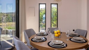 A dining table set for four with a clear view of the outdoors through large windows. - Unforgettable Tinos Beach house III (Tinos)