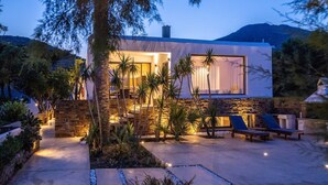 A modern house with a stone facade, large windows, and a patio area with lounge chairs and a pool. - Unforgettable Tinos Beach house III (Tinos)