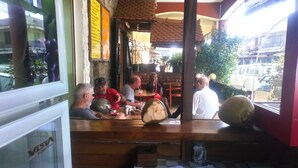A restaurant with wooden tables and chairs, a visible menu board, and a view of the street outside. - CENTRAL HOTEL  (Antsiranana)