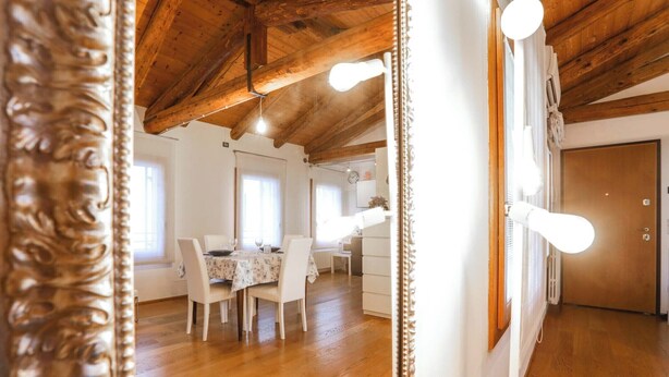Un comedor con techo de madera, una mesa con sillas y una pared blanca con una lámpara.