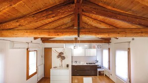 Una habitación amplia con un alto techo de madera, una zona de cocina con electrodomésticos modernos y un gran ventanal que proporciona luz natural.