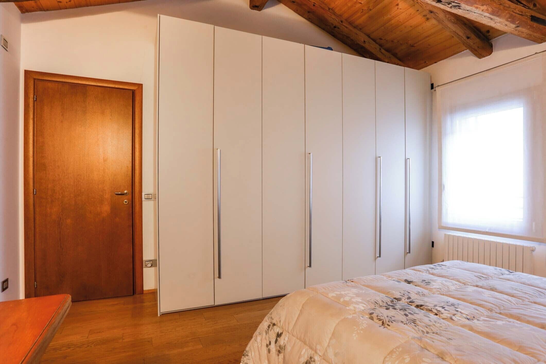 A bedroom with a wooden door, a bed with a floral duvet, and a large wardrobe with sliding doors.