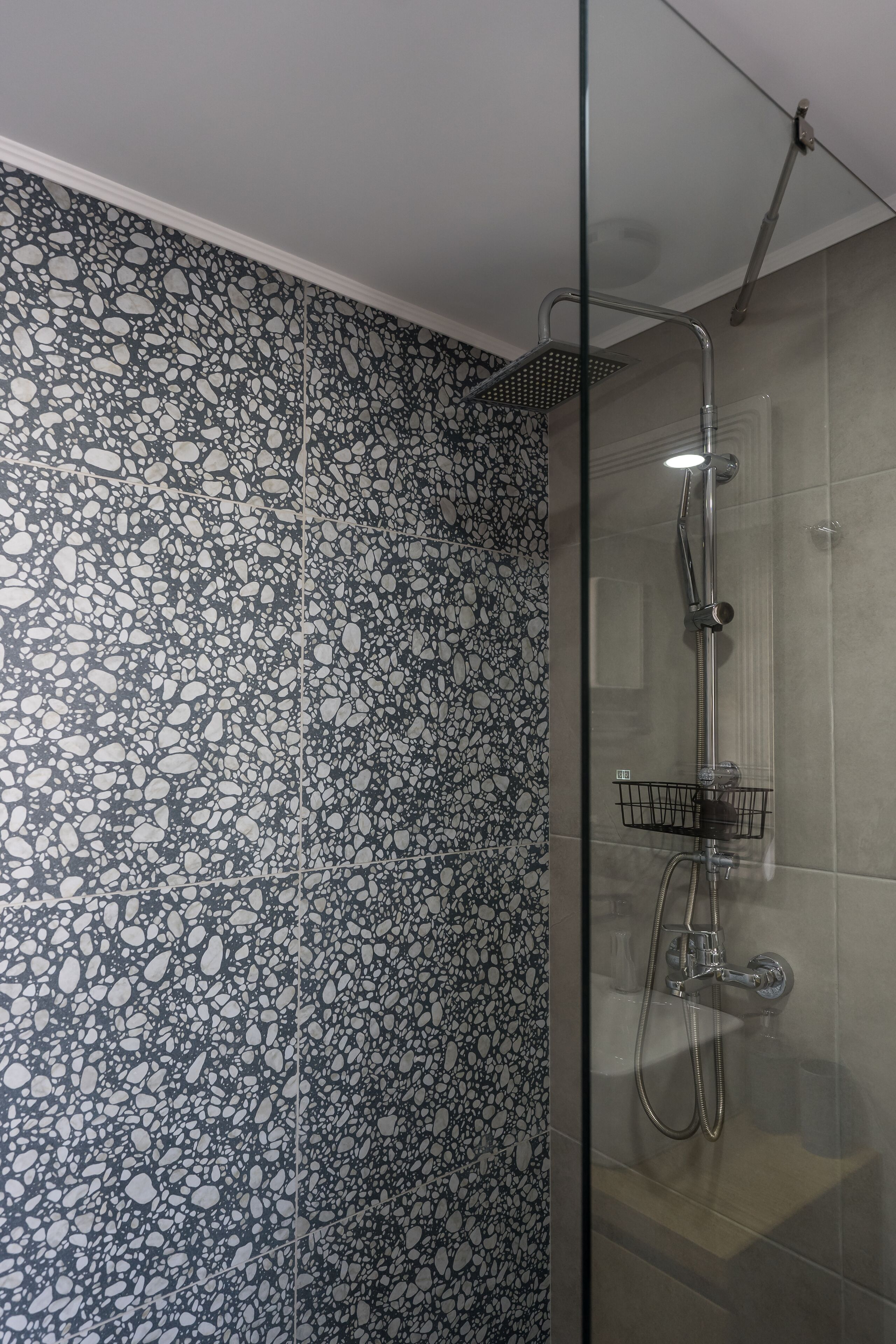 A shower with a glass door, a metal showerhead, and a black shower caddy.
