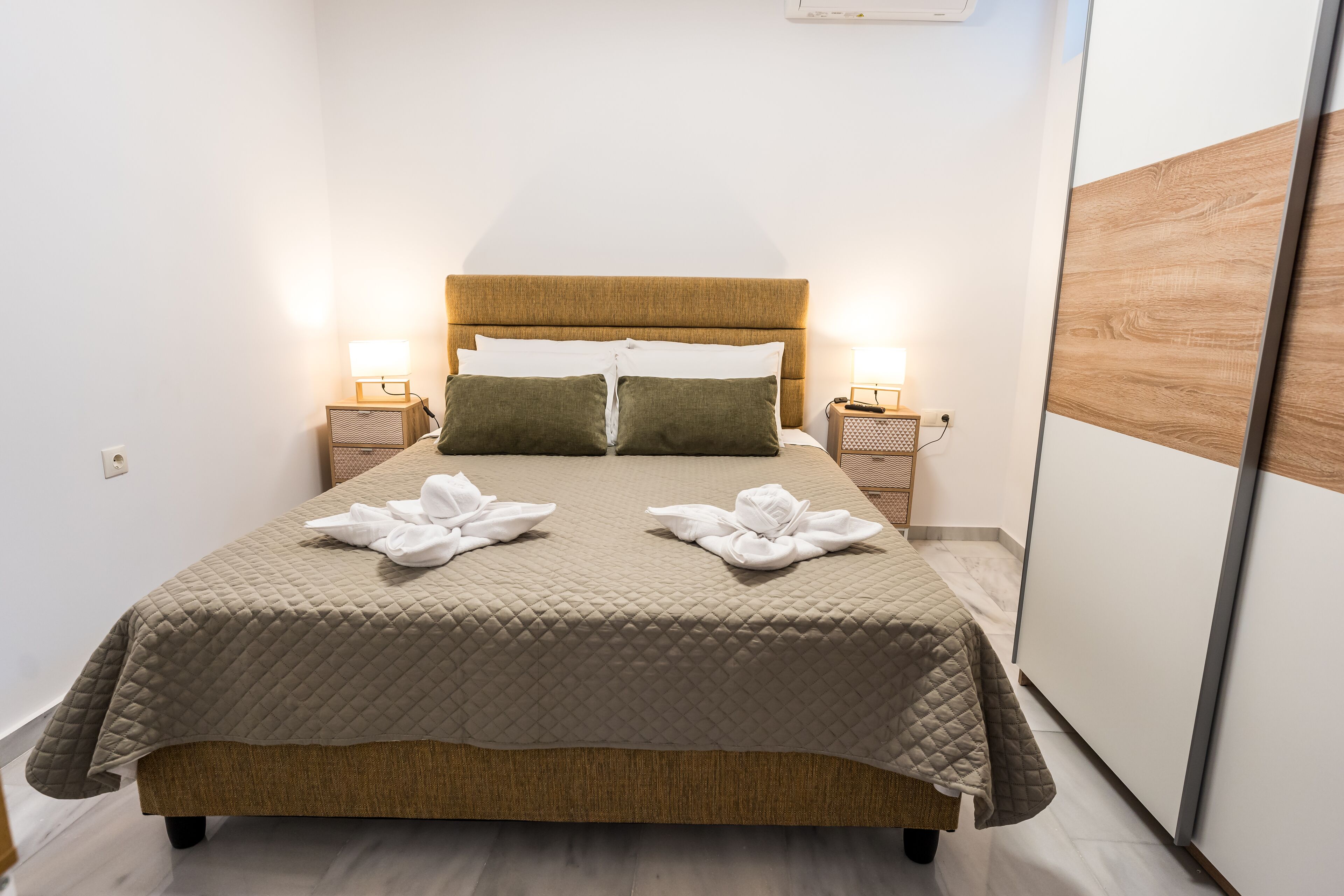 Una cama bien hecha con cubrecama acolchado, dos lámparas de noche y un cabecero de madera.