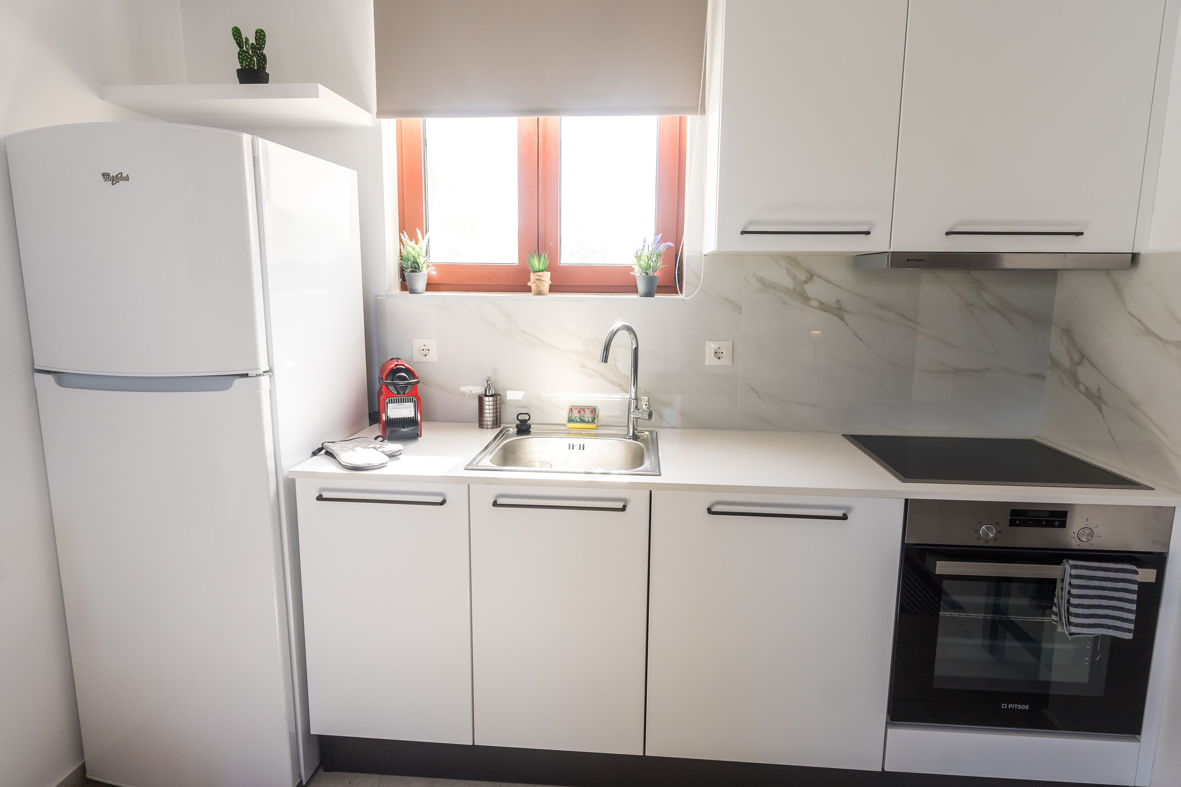 Een moderne keuken met witte kasten, een ingebouwde oven, een spoelbak en een raam met plantenpotten.