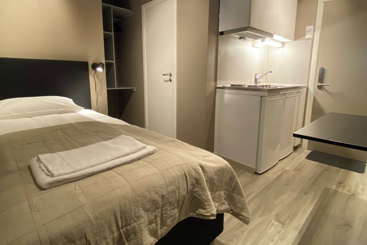 A compact hotel room with a bed, a small kitchenette, and a separate dining area.
