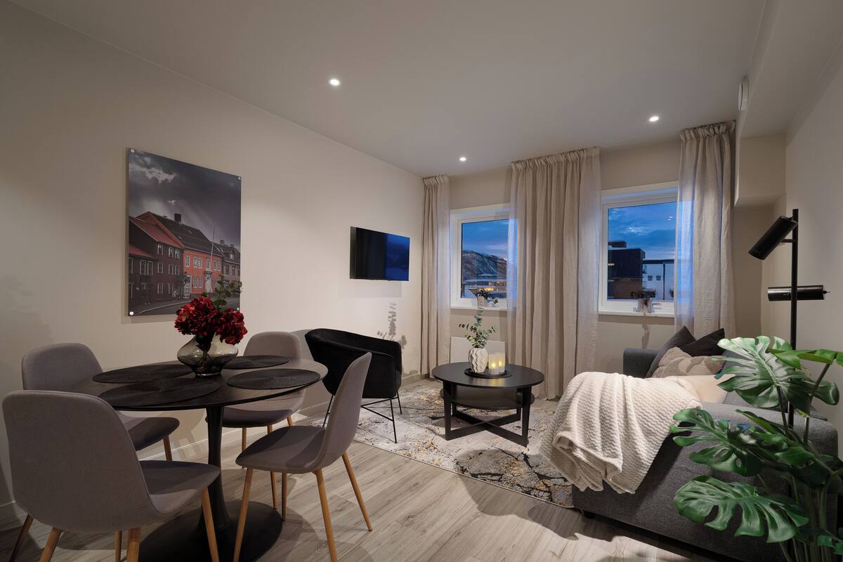 A modern living room with a dining area, a sofa, a coffee table, and a large window with curtains.