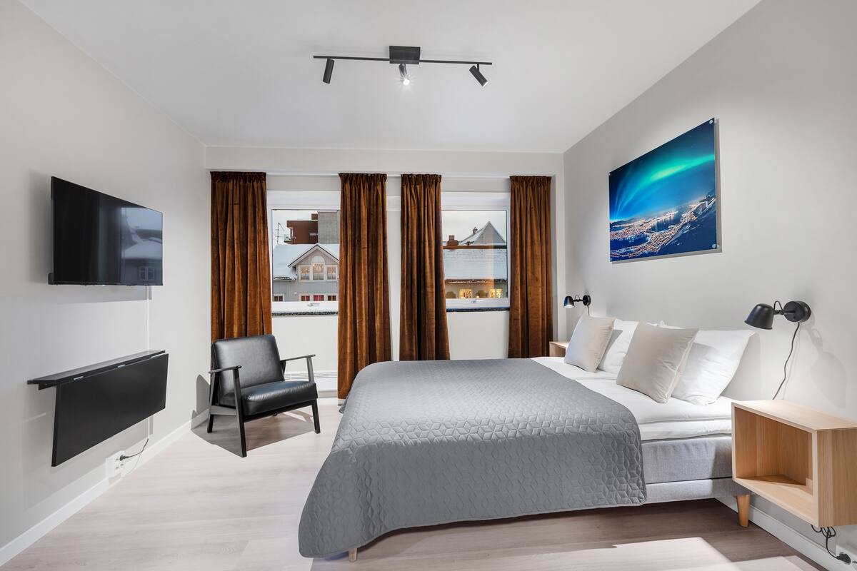 A modern bedroom with a bed, a TV, a chair, and a desk.