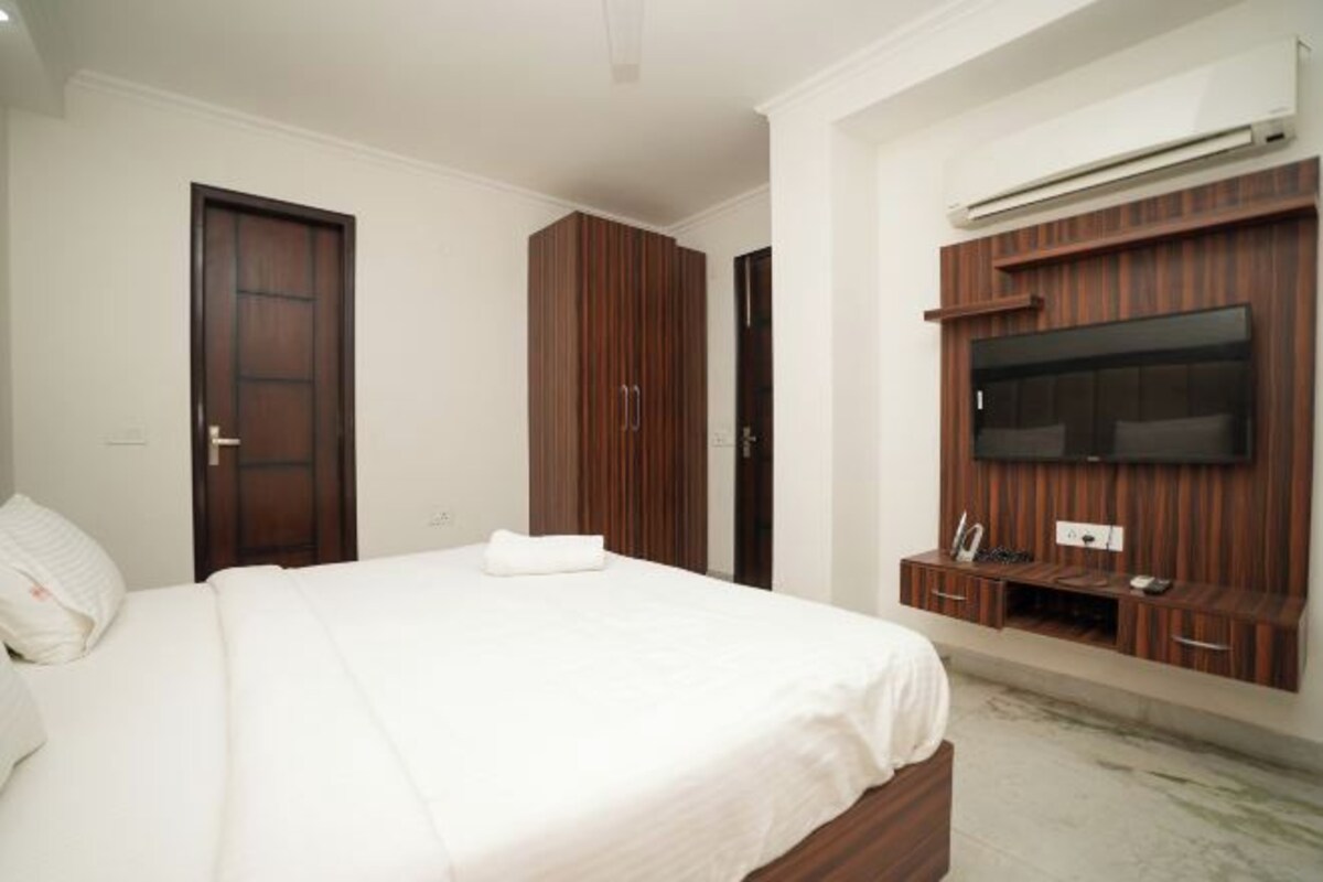 A bedroom with a bed, a wardrobe, a TV mounted on the wall, and a small desk area.