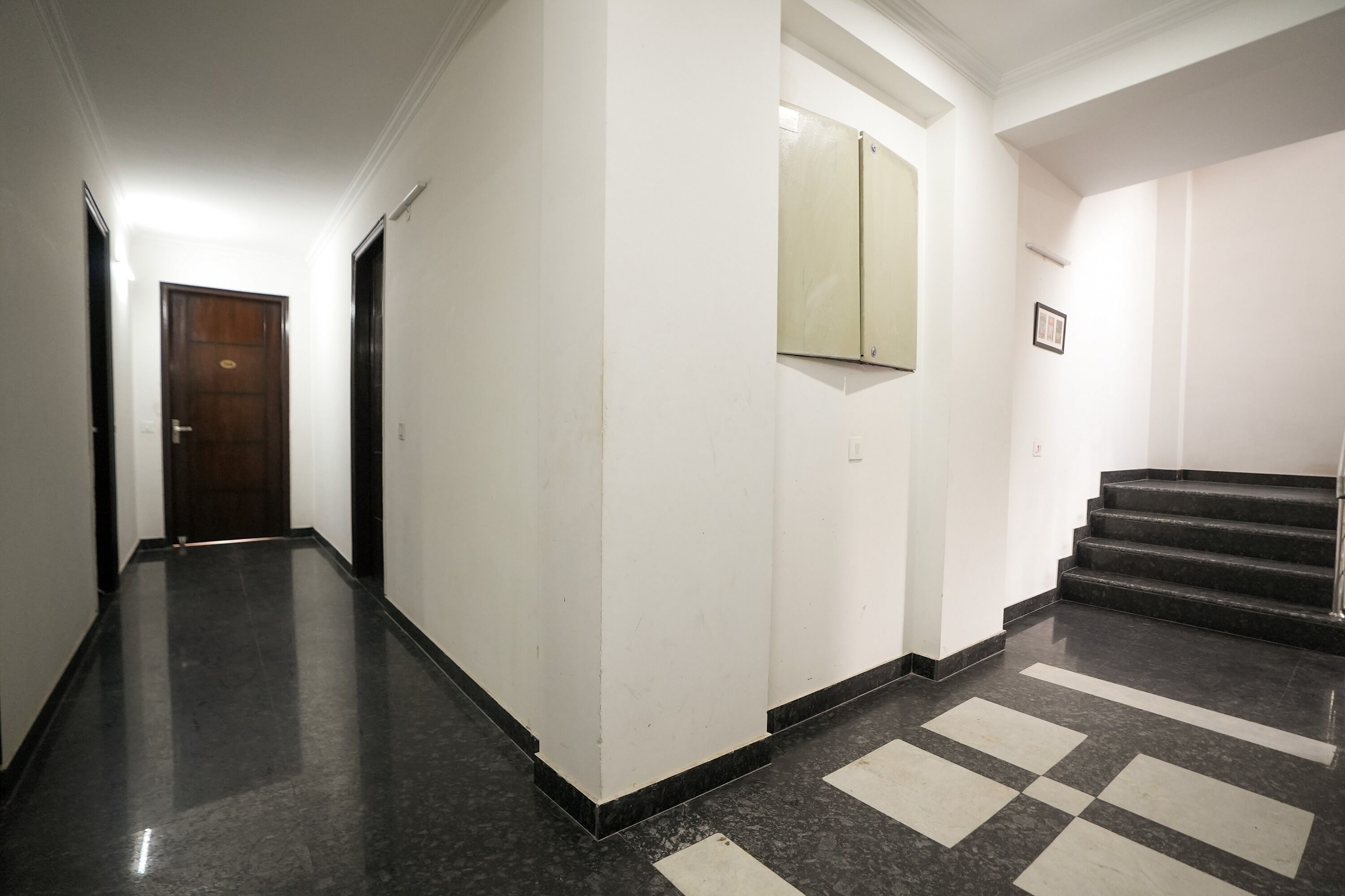 A hallway with a dark marble floor, white walls, and a wooden door at the end.