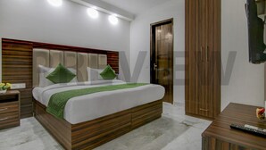 Un dormitorio moderno con cabecera de madera, cama con almohadas verdes, mesita de noche, armario y televisor montado en la pared.
