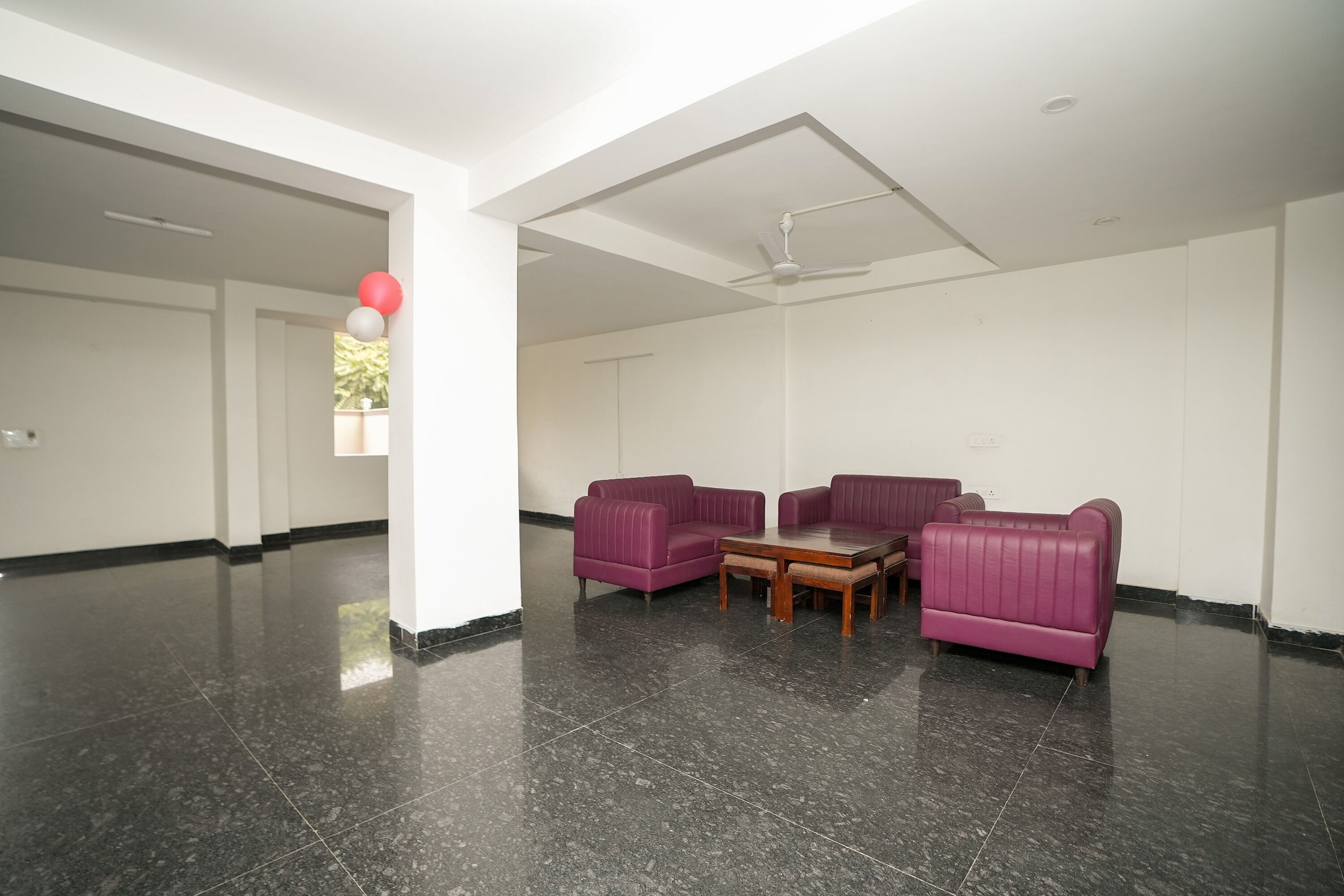A spacious room with a black marble floor, white walls, and purple sofas arranged around a wooden coffee table.