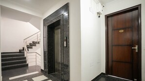 Un hall moderno de hotel con piso de mármol, una escalera, un ascensor y una puerta de madera.