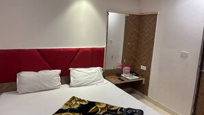 A hotel room with a bed, two pillows, a bedside table with a mirror, and a red headboard.