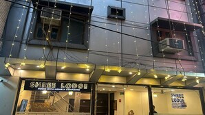 A building with a sign for 'Shree Lodge' indicating rooms available, ticket facility, and taxi for airport.