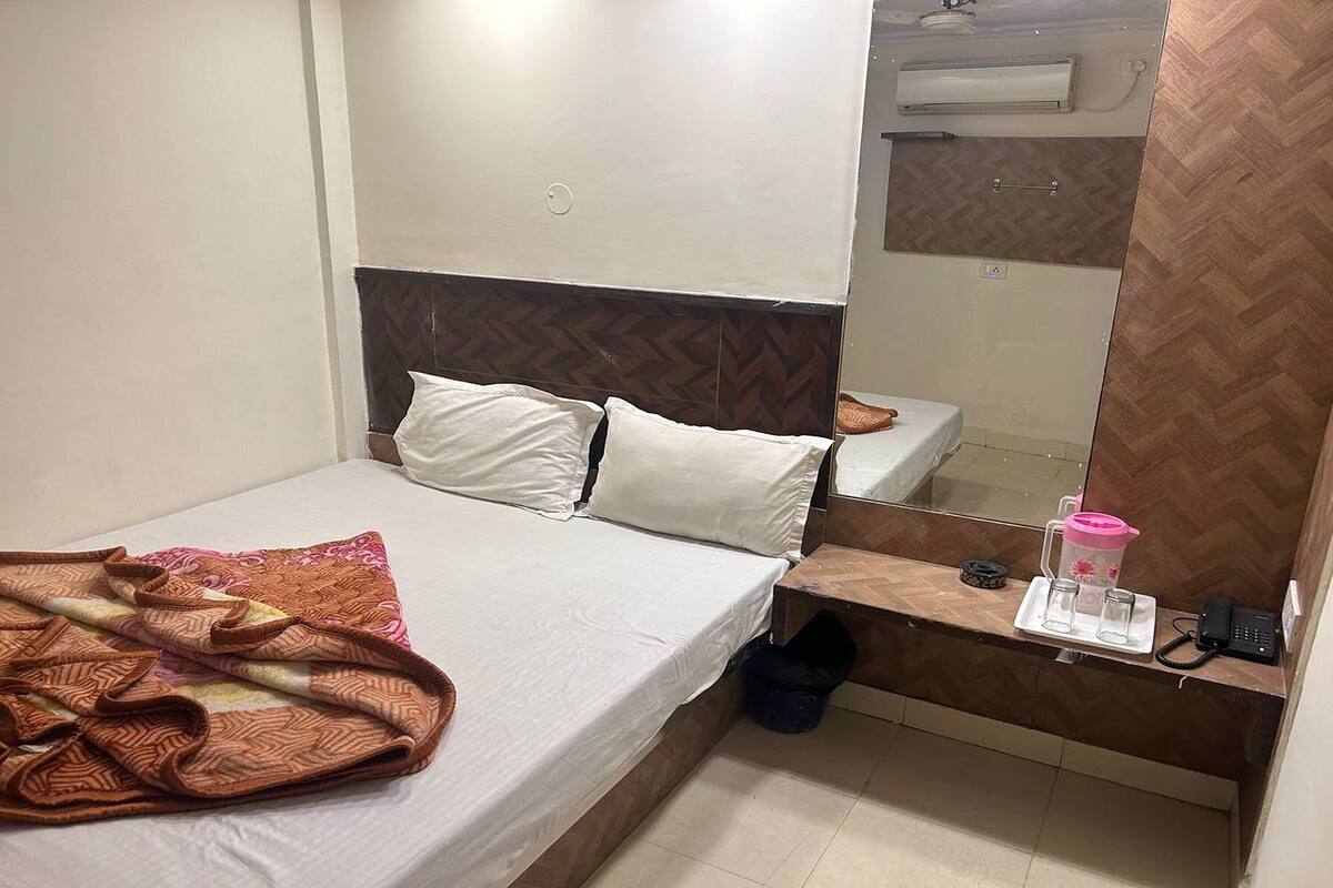 Un dormitorio con una cama, una mesita de noche con un teléfono y una botella de agua rosa, y un espejo sobre la cama.